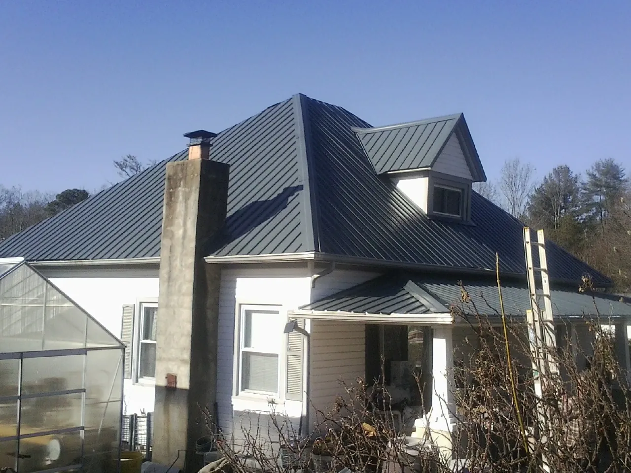 Dark blue standing seam metal roof on a white farmhouse with dormer — Slate & Tile Roof Repair by Roofing Brothers in Sumpter