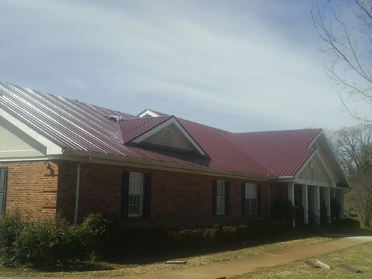 Red metal roof with gabled entries on a long brick building, from a Hail Damage Roof Repair job in Sumpter