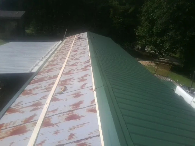 Old rusted panels beside newly installed green metal roofing — Wind Damage Roof Repair by Roofing Brothers in Sumpter