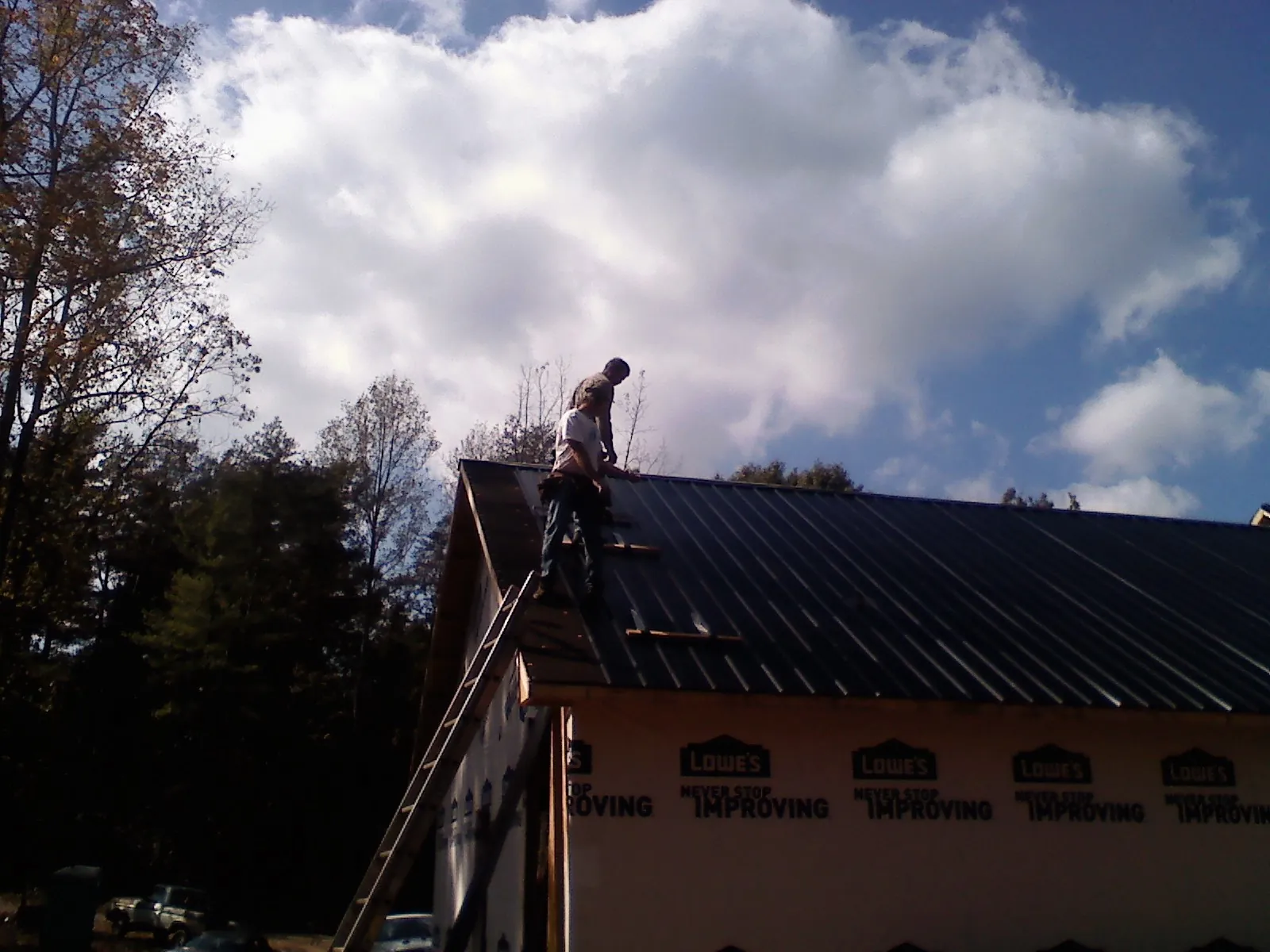 Roofer fastening dark metal panels high against a cloudy sky, from a Roof Inspection job in Sumpter