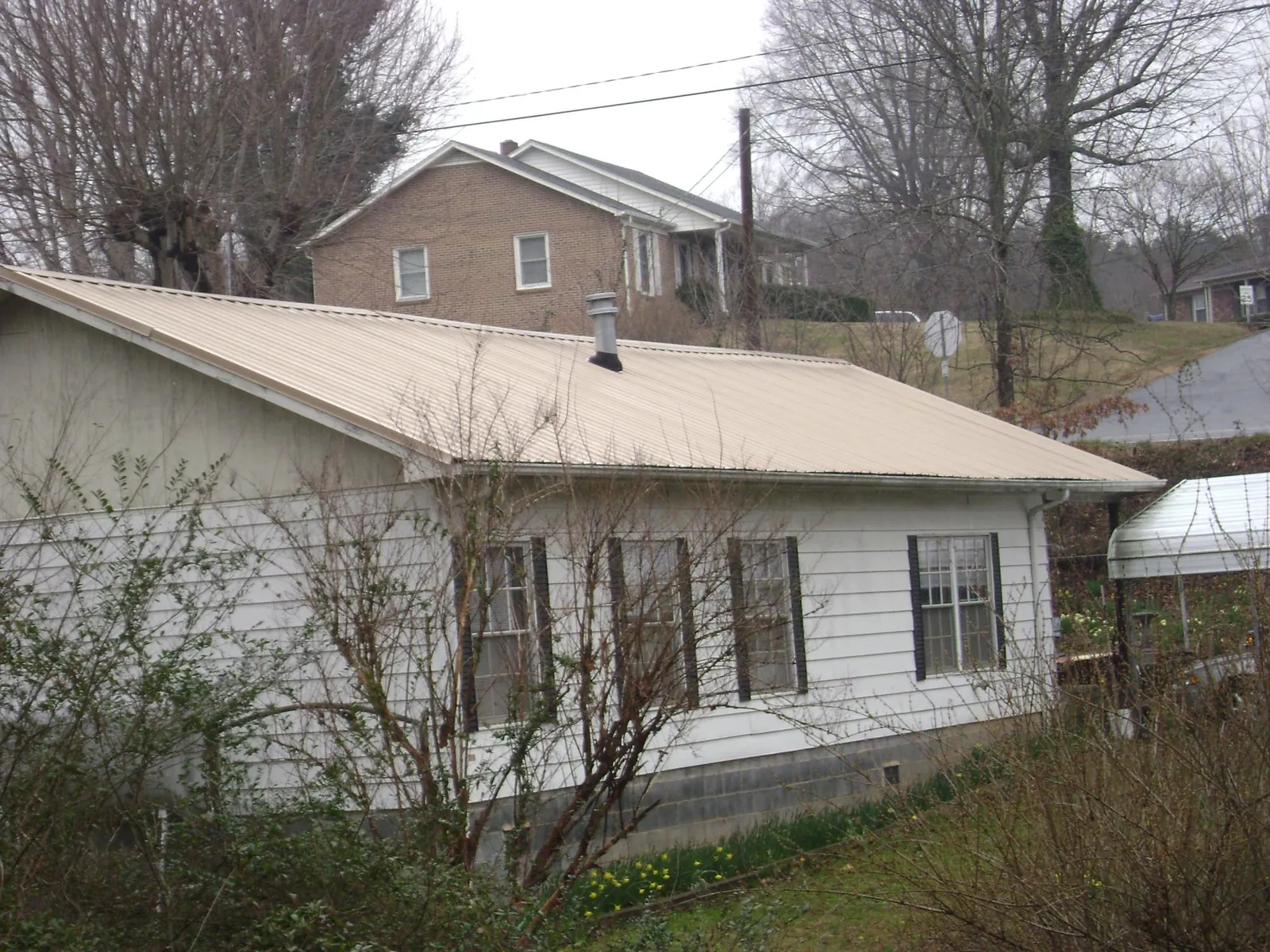 Tan metal roof on a white sided house set into a hillside — Commercial Roofing by Roofing Brothers in Sumpter
