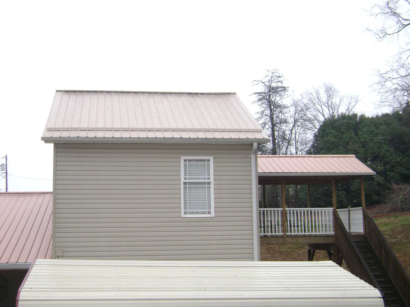 Tan metal roofs on a two story addition and attached porch, from a Roof Replacement job in Sumpter
